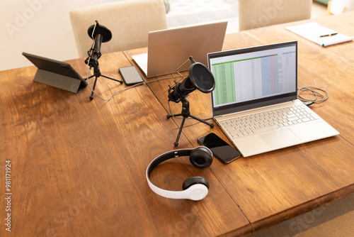 Podcasting setup with laptops, microphones, and headphones on wooden table, copy space