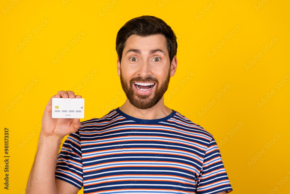 Portrait of impressed guy with bristle wear striped t-shirt presenting debit card astonished staring isolated on yellow color background Portrait of impressed guy with bristle wear striped t-shirt presenting debit card astonished staring isolated on yellow color background