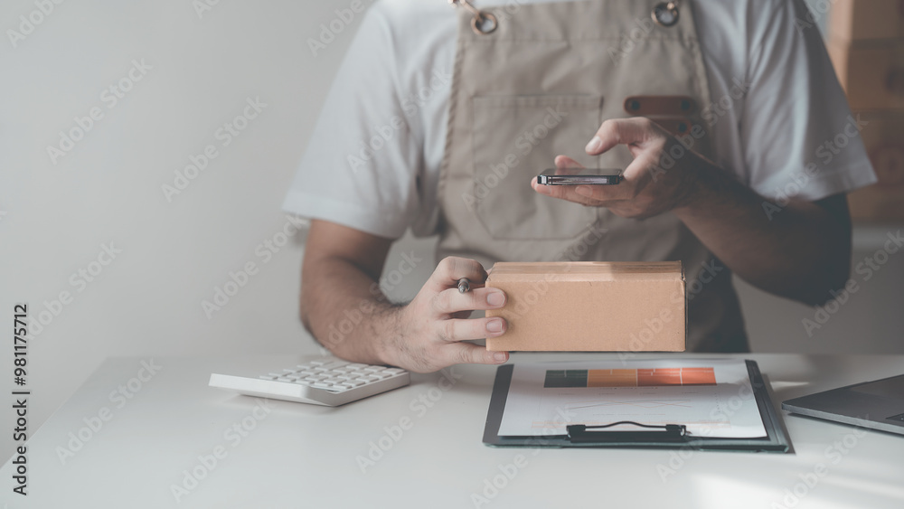 Fototapeta premium Male SME owner, entrepreneur, works boxes and checks online orders. To prepare to pack boxes to sell to customers, online SME business ideas Close-up pictures