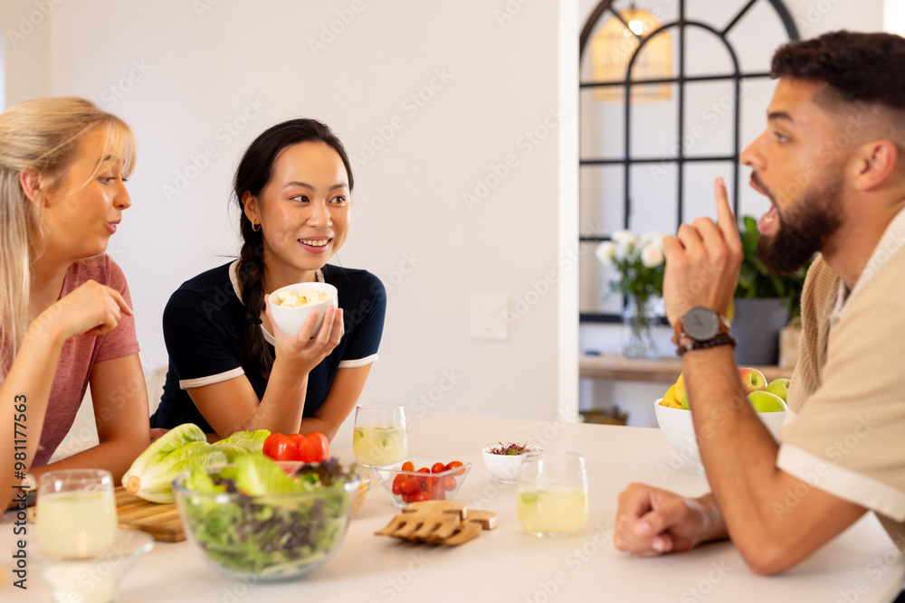 Friends enjoying healthy meal and conversation around kitchen table with salad Friends enjoying healthy meal and conversation around kitchen table with salad