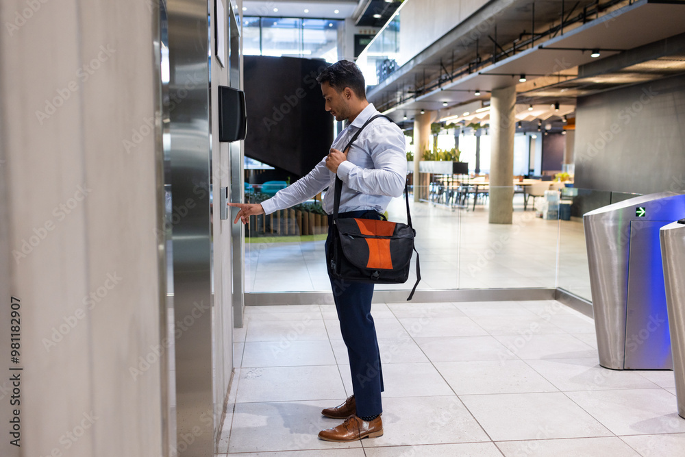 Fototapeta premium Businessman with briefcase pressing elevator button in modern office building