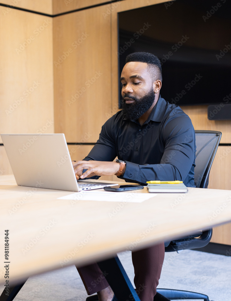 Working on laptop, man sitting at desk in modern office setting Working on laptop, man sitting at desk in modern office setting