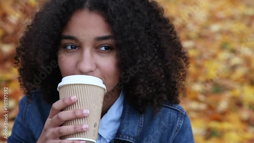 Beautiful mixed race African American girl teenager young woman wearing a blue denim jacket outside drinking coffee or tea