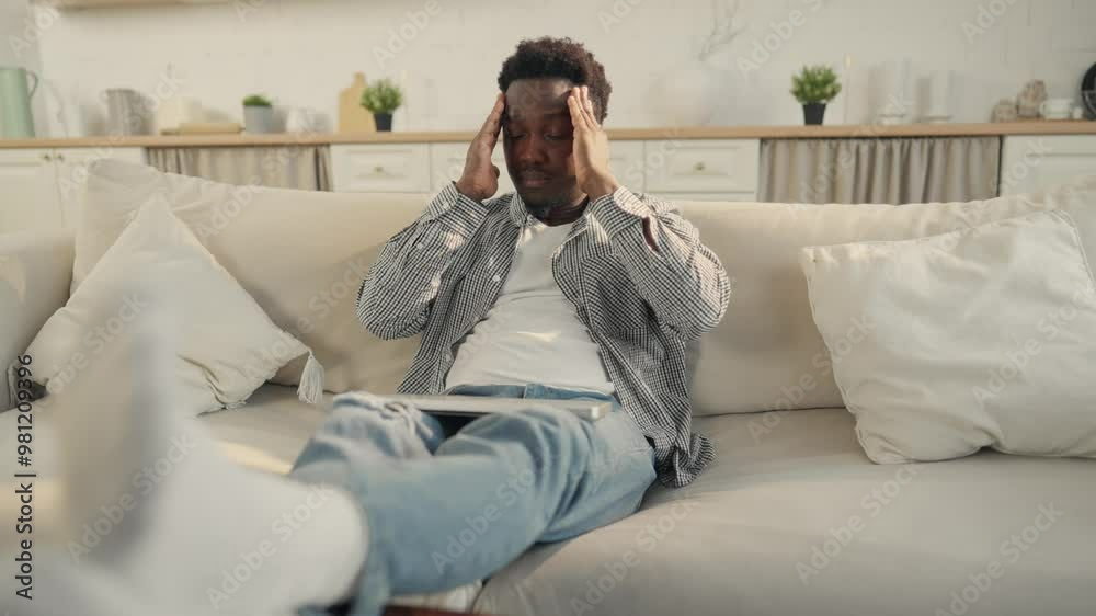 Young African American man feeling headache after laptop use at home, portrait. Disease by overuse of computer, self-massage of temples and neck, osteochondrosis, health problems of modern people