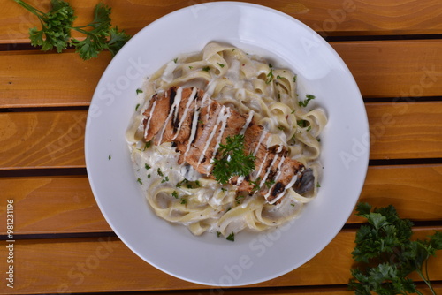 Fettuccine Alfredo with chicken served in a bowl, captured from an angle view. The creamy sauce and pasta create an appealing presentation for a restaurant setting. photo