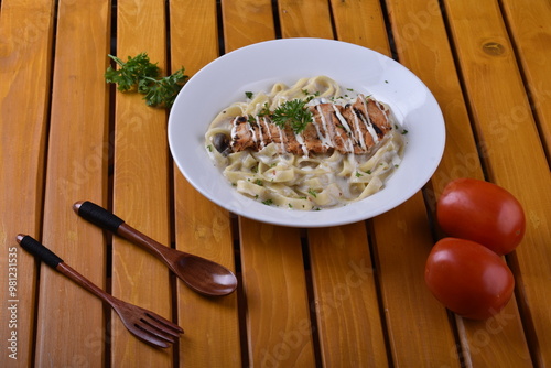 Fettuccine Alfredo with chicken served in a bowl, captured from an angle view. The creamy sauce and pasta create an appealing presentation for a restaurant setting. photo