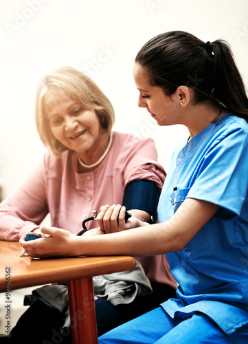 Senior woman, nurse and blood pressure at table for vital signs, assessment and monitor of health. Elderly patient, smile and caregiver with apparatus in home for medical exam, evaluation and support