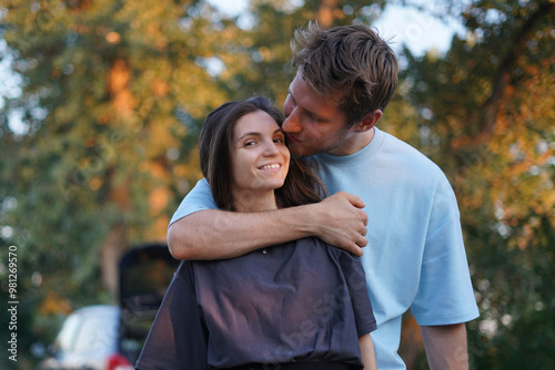 woman in a black shirt embraces a man in a blue shirt as they stand in a forest. The sun shines behind them, creating a warm, golden glow