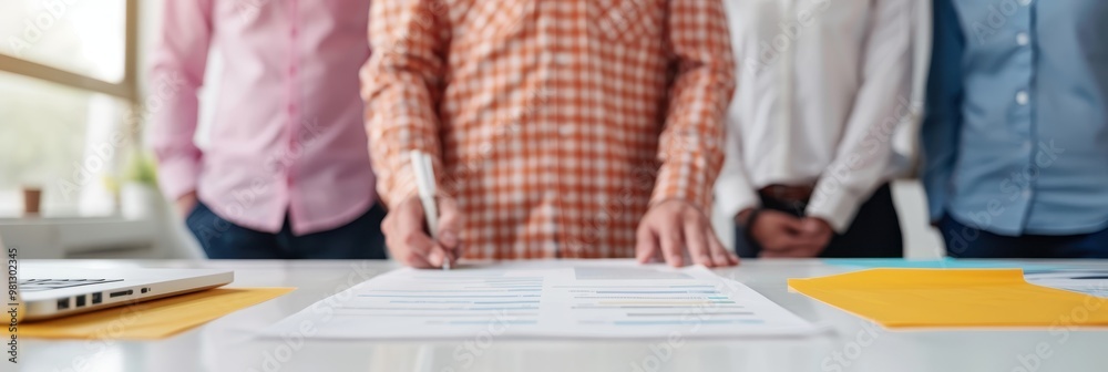 Group of business professionals standing around a table, reviewing financial documents and data charts during a meeting, with a focus on strategy and collaboration. Group of business professionals standing around a table, reviewing financial documents and data charts during a meeting, with a focus on strategy and collaboration.