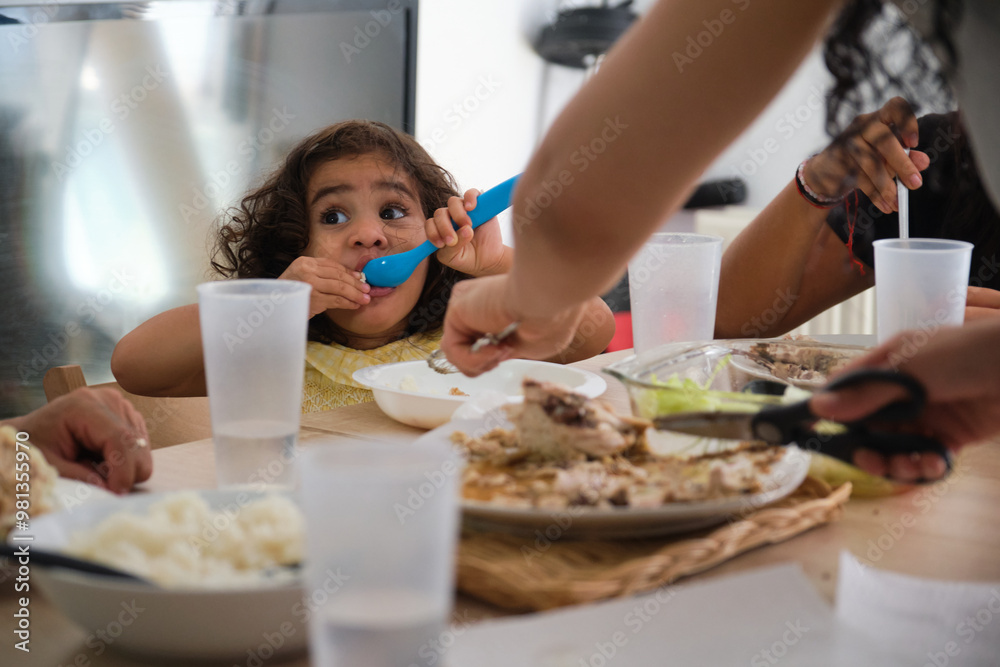 Mother is serving her daughter lunch at their kitchen table, while the rest of the family eats Mother is serving her daughter lunch at their kitchen table, while the rest of the family eats