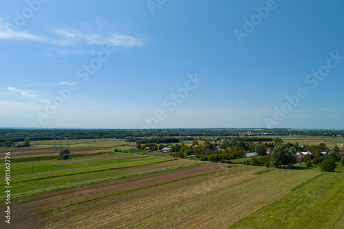 A beautiful aerial view showcasing lush green fields and a serene village under a clear blue sky, perfect for landscape and nature enthusiasts.