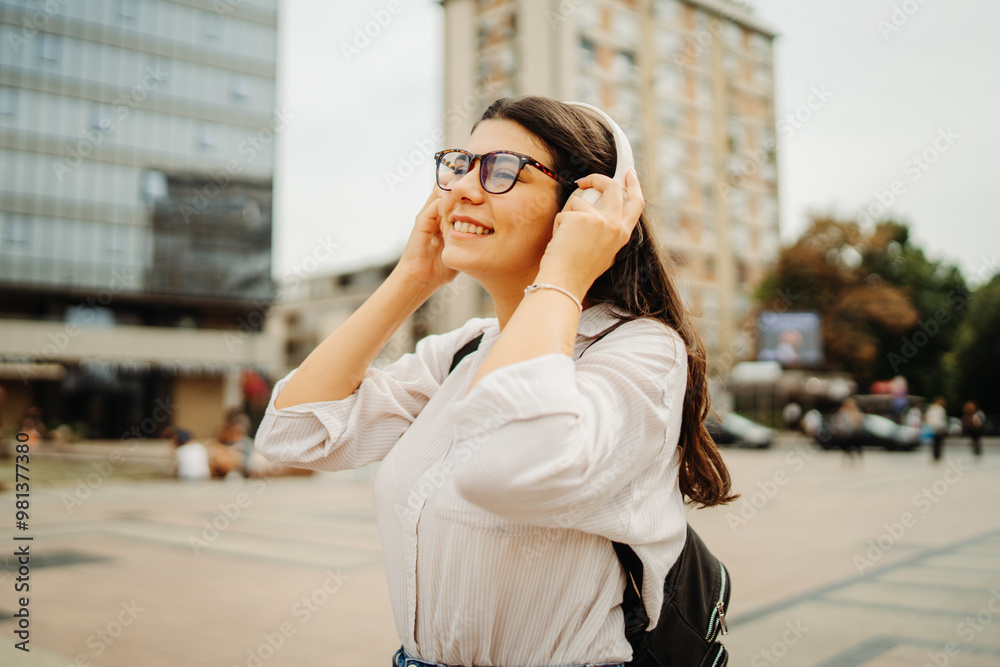 Fototapeta premium Young caucasian woman listening to music or audio book in the city