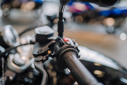 Fotografi Munich, Germany - September 13, 2024 - Close-up of a motorcycle handlebar showing controls and buttons, with a blurred background of other bikes in a showroom
