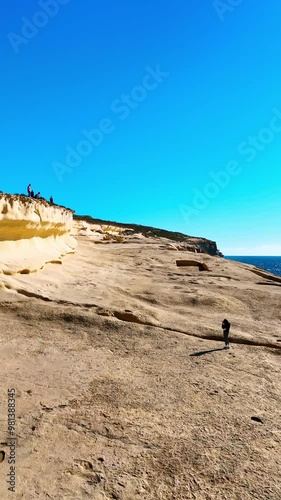 Tourists walk near the Xlendi Tower in Gozo Island, Malta. Rocky shore and blue waterscape of the Mediterranean Sea. Vertical video. photo