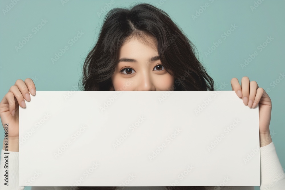 Cheerful young Asian woman standing behind blank white banner Cheerful young Asian woman standing behind blank white banner