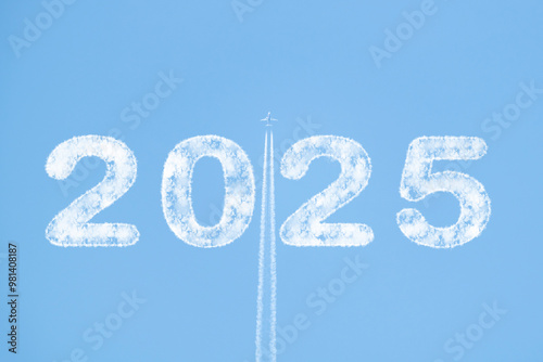 Plane soaring through blue sky with 2025 text in clouds and white smoke trail photo