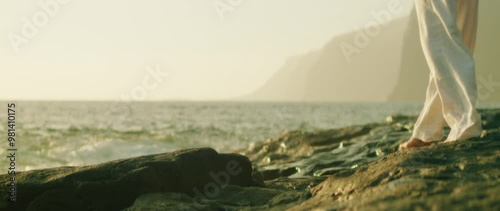 Close-up of feet on rugged stones near the ocean waves at sunset creating a peaceful natural atmosphere
