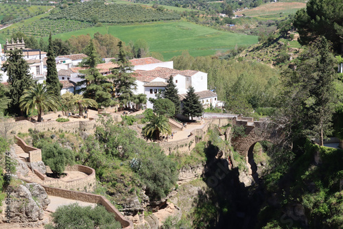 Tourists walking on bridge overlooking green valley in ronda spain