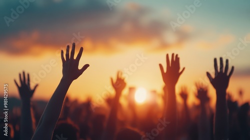 A crowd raises their hands in celebration or support against a vibrant sunset sky, capturing a moment of unity and expression.