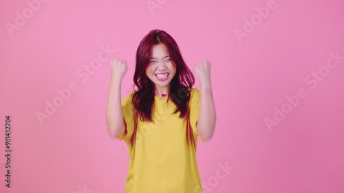A young Asian woman with vibrant red hair, wearing a yellow t-shirt, stands against a pink background, joyfully exclaiming Wow Her wide smile and excitement create a lively and happy atmosphere