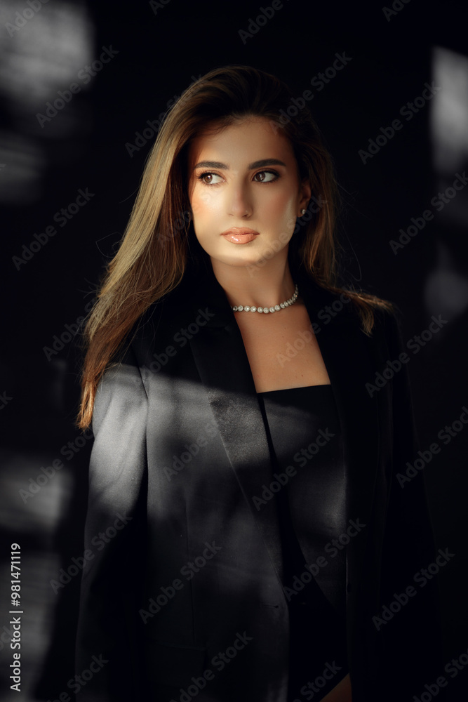 Profile portrait of a elegant smiling young woman in black suit, looking at camera, posing in studio. Profile portrait of a elegant smiling young woman in black suit, looking at camera, posing in studio.