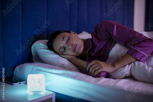 Woman sleeping in bed with modern digital alarm clock counting down time to awakening on bedside table