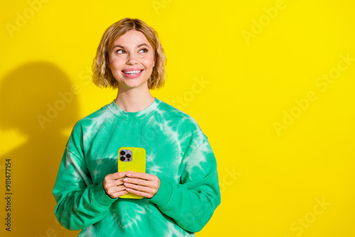 Photo of shiny thoughtful lady dressed tie dye sweatshirt communicating modern gadget looking empty space isolated yellow color background