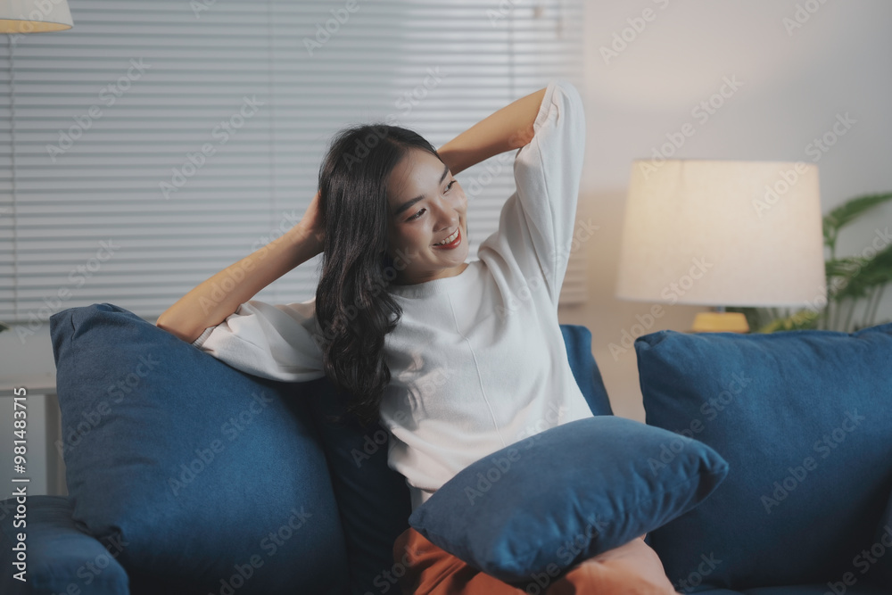 Smiling young woman relaxes on her living room couch, stretching her arms and enjoying a peaceful evening at home Smiling young woman relaxes on her living room couch, stretching her arms and enjoying a peaceful evening at home