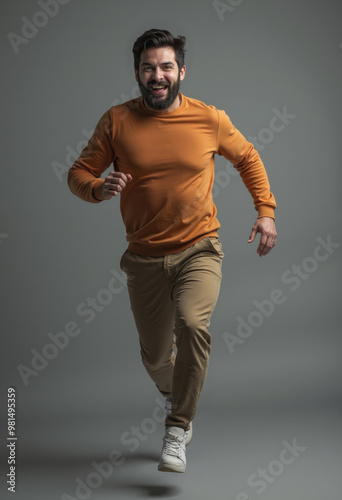 Enthusiastic man running joyfully in casual outfit across minimalistic gray backdrop during vibrant photoshoot