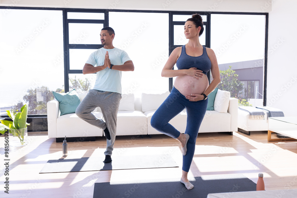 At home, Multiracial couple, Pregnant woman and man practicing yoga together on mats in living room At home, Multiracial couple, Pregnant woman and man practicing yoga together on mats in living room
