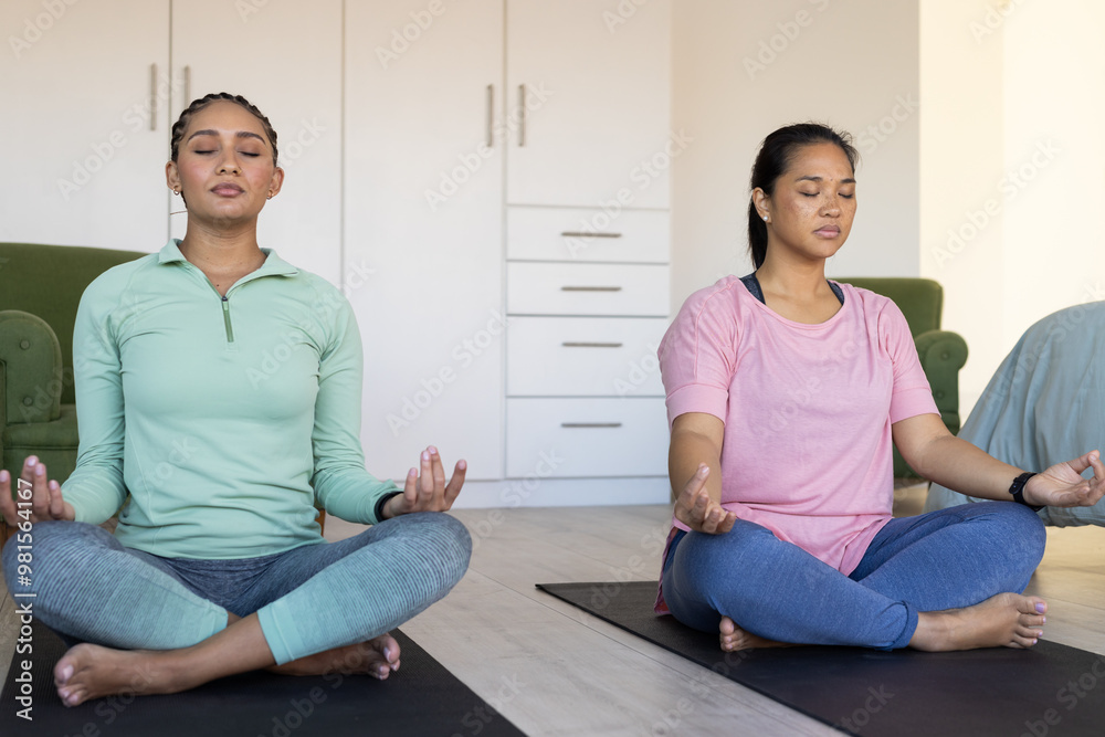 Meditating on yoga mats, two women friends practicing mindfulness at home Meditating on yoga mats, two women friends practicing mindfulness at home