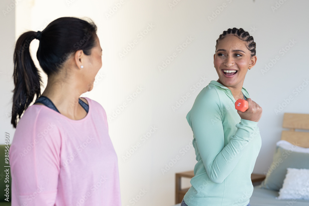 Exercising at home, women friends smiling and lifting dumbbells together in living room Exercising at home, women friends smiling and lifting dumbbells together in living room