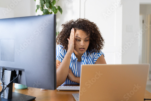 Working from home, woman with curly hair looking frustrated at laptop and desktop monitor