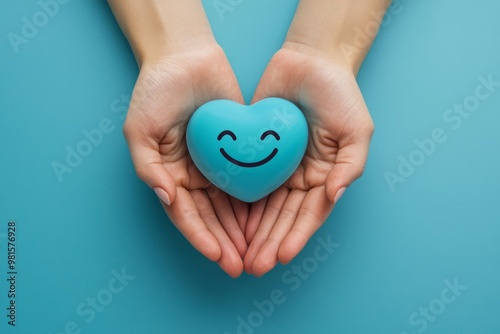 Close-up of hands gently holding a blue heart with a smiley face on a pastel blue background, offering a sense of happiness and warmth, perfect for mental health awareness and positivity photo