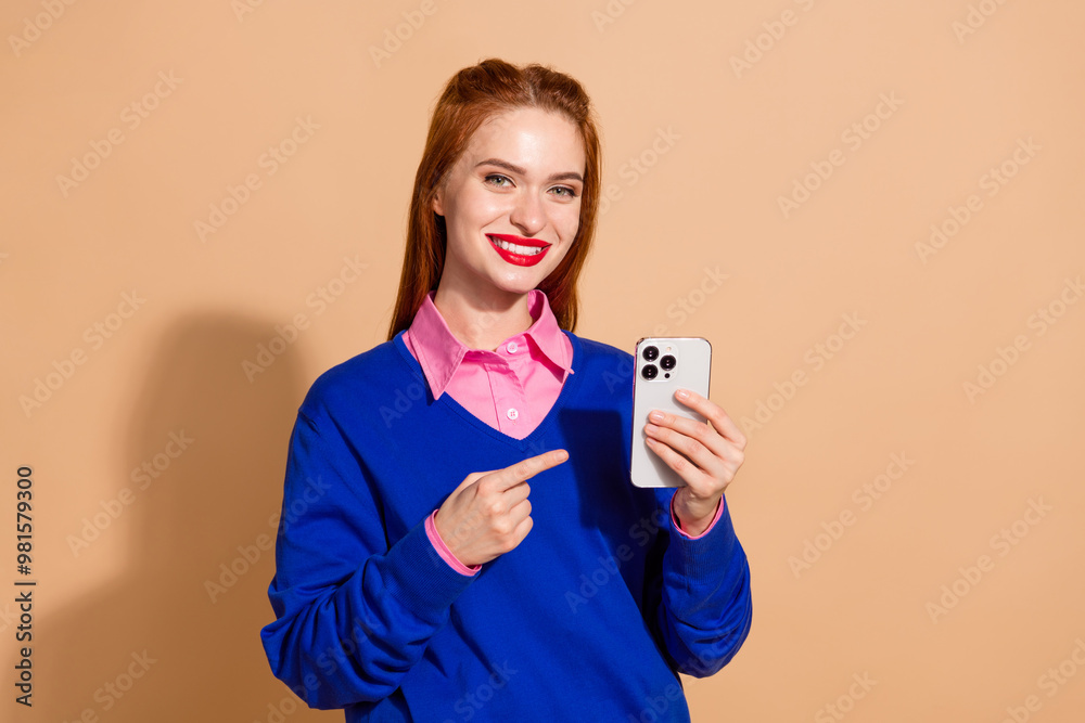 Photo of cheerful sweet lady wear sweater pointing finger modern gadget empty space isolated beige color background Photo of cheerful sweet lady wear sweater pointing finger modern gadget empty space isolated beige color background