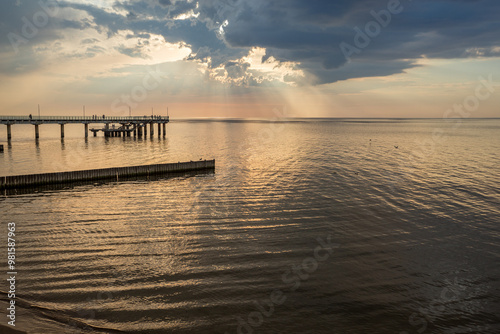 The Baltic Sea at sunset. A beautiful seascape with orange and gray clouds and a pier in the foreground. The city of Zelenogradsk and the embankment