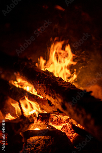 A campfire burns brightly at night, illuminating the surrounding area with flickering flames and glowing embers