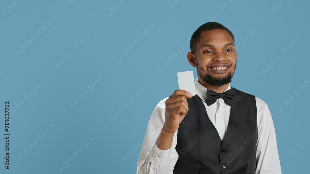 Classy hotel bellboy in tuxedo giving the room access key card to guest after check in, offering excellent concierge services at holiday resort. Employee working in hospitality industry. Camera A. Classy hotel bellboy in tuxedo giving the room access key card to guest after check in, offering excellent concierge services at holiday resort. Employee working in hospitality industry. Camera A.