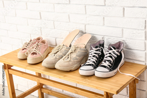 Stylish shoes and orthopedic insoles on wooden rack shoe near light brick wall