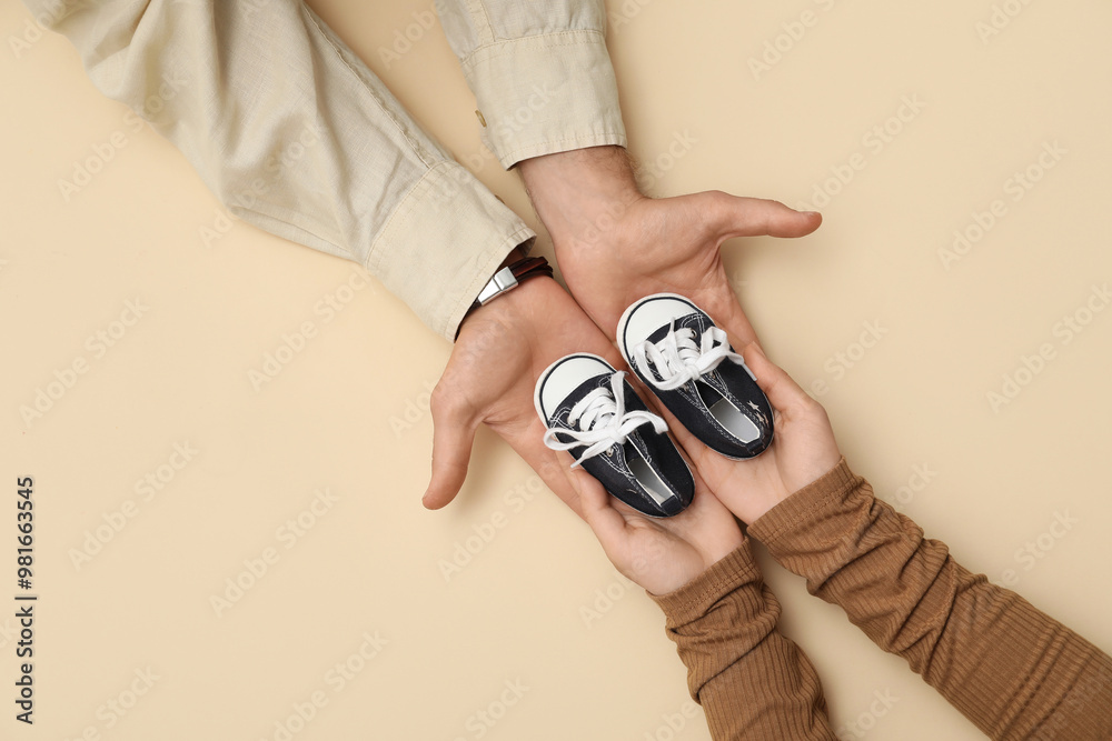 Couple with baby booties on beige background, top view