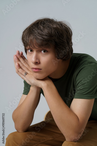Canvas Print A young man in a green shirt is sitting on a chair with his hands on his knees