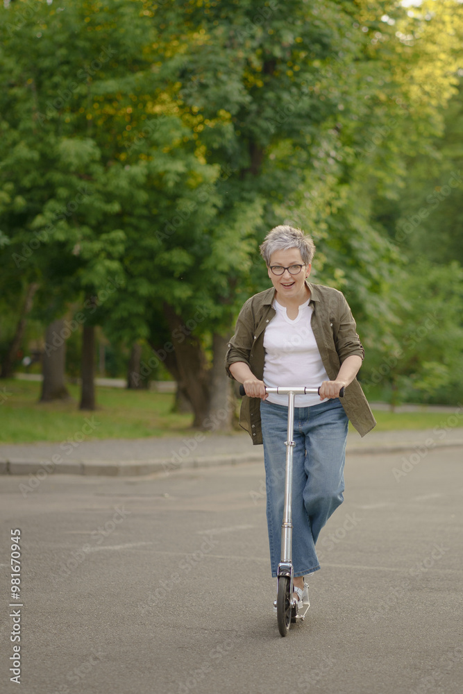 Obraz premium A woman is riding a scooter in a park. She is wearing a green shirt and blue jeans