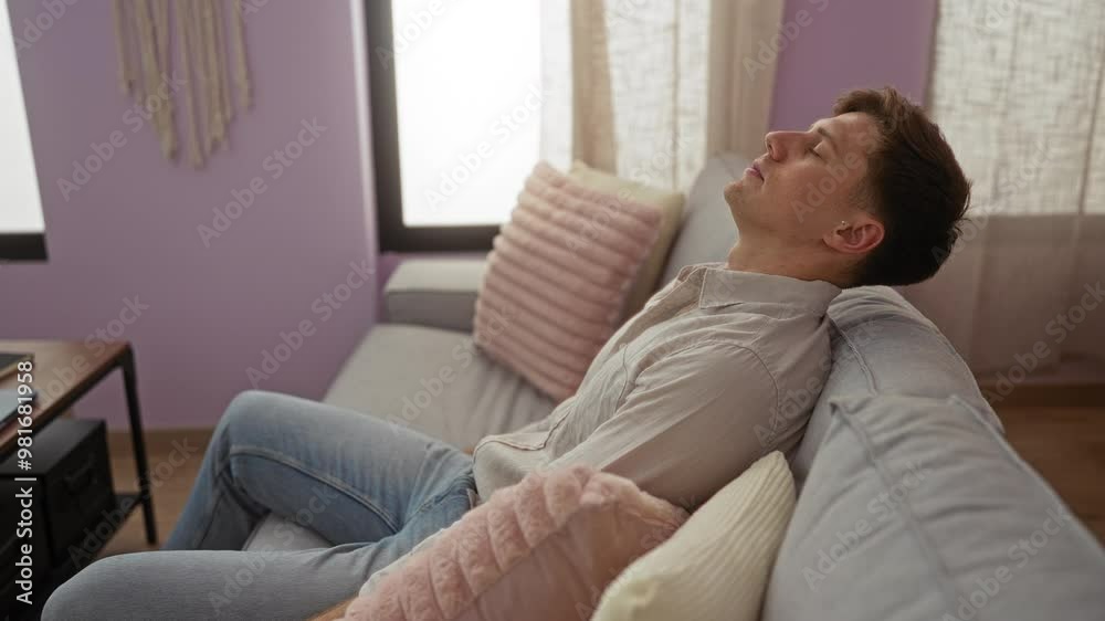 Young man relaxing on a couch in a cozy living room with pastel pillows and neutral decor creating a peaceful indoor setting Young man relaxing on a couch in a cozy living room with pastel pillows and neutral decor creating a peaceful indoor setting