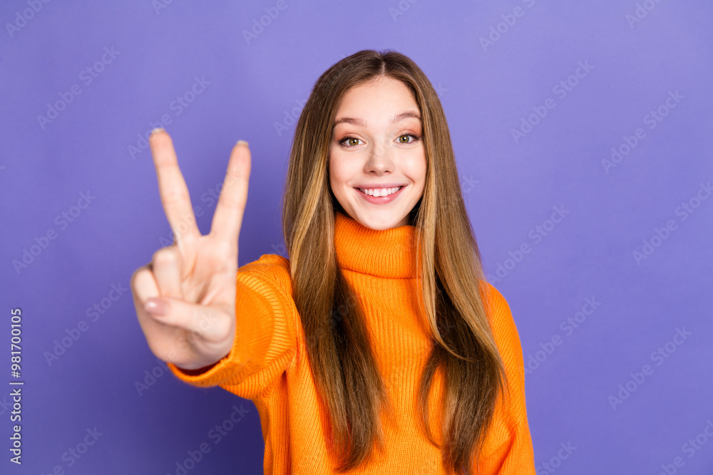 Portrait photo of youth charming blonde hair cute happy smile girl showing for you v sign trend in orange turtleneck isolated on violet color background Portrait photo of youth charming blonde hair cute happy smile girl showing for you v sign trend in orange turtleneck isolated on violet color background