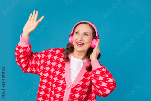 Photo portrait of attractive retired woman dancing headphones dressed stylish pink print clothes isolated on blue color background photo