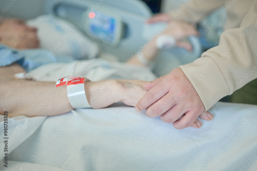 Obraz premium Young woman keeps company and accompanies an unrecognizable elderly woman by holding her hand during her stay in a hospital room