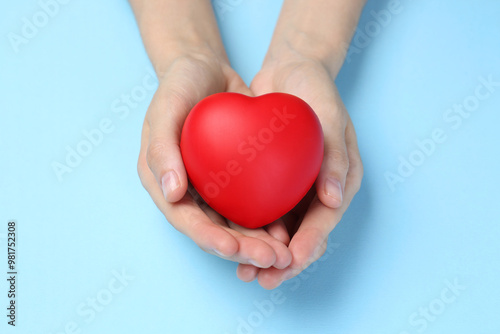 Woman holding red heart on light blue background, closeup