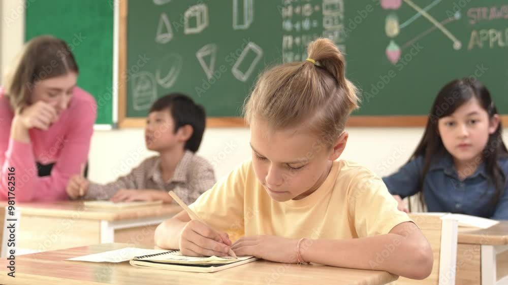 Caucasian smart child smiling at camera while doing classwork at classroom while happy multicultural student doing test or writing note in classroom at elementary class. Education concept. Pedagogy. Caucasian smart child smiling at camera while doing classwork at classroom while happy multicultural student doing test or writing note in classroom at elementary class. Education concept. Pedagogy.