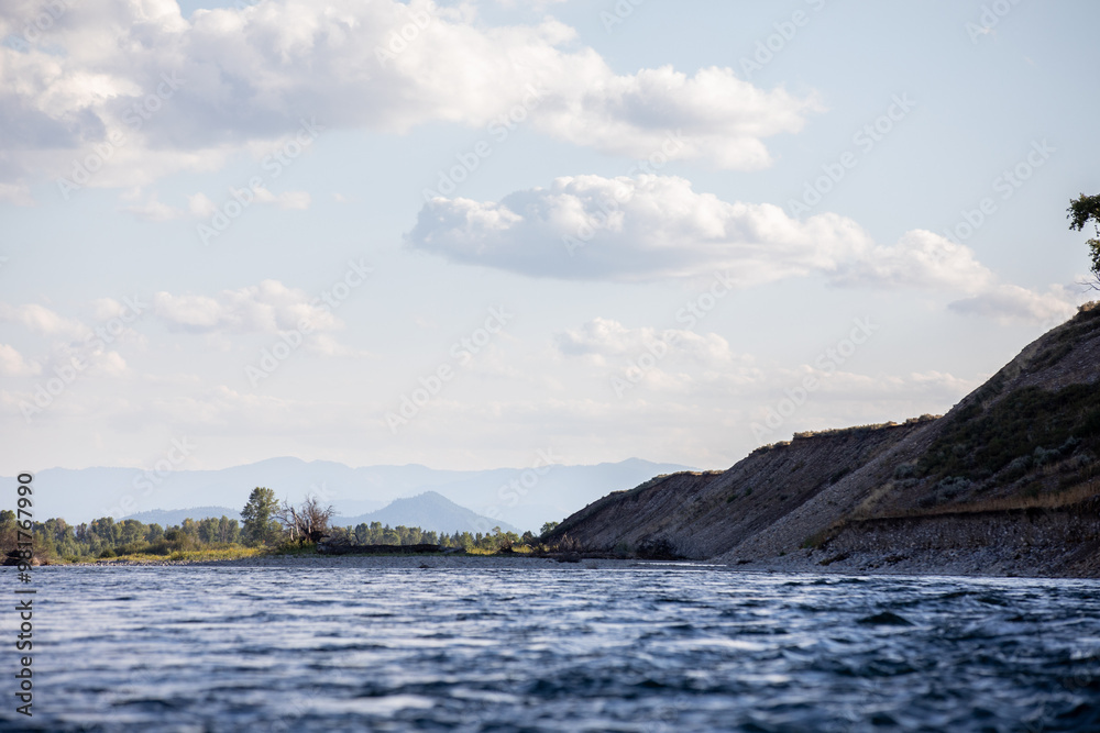 Photo taken from the middle of Snake River at The Grand Tetons National Park, View from water surface looking up at blue mountains on horizon light fluffy day. Photo taken from the middle of Snake River at The Grand Tetons National Park, View from water surface looking up at blue mountains on horizon light fluffy day.