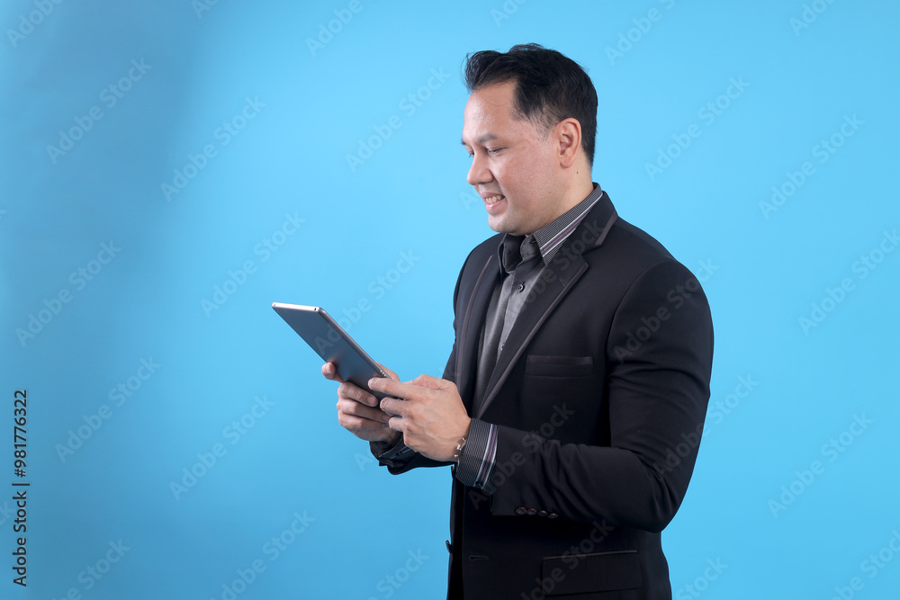 Side view of Asian businessman using digital tablet isolated on blue background Side view of Asian businessman using digital tablet isolated on blue background